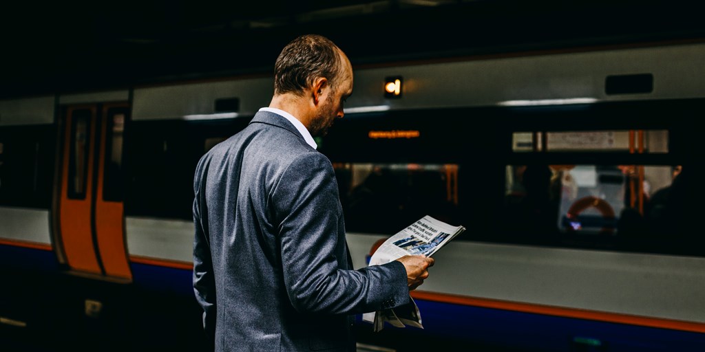 Man waiting to take the train reading a newspaper